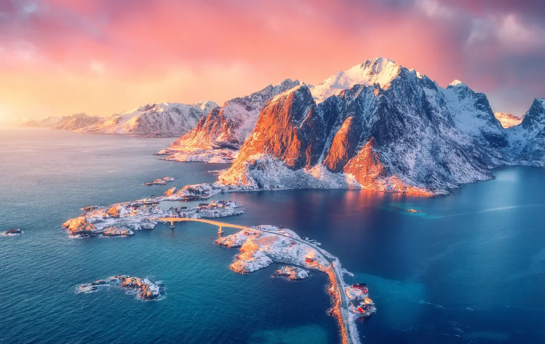 Natural Pharmaceuticals OmegaMarine™ Premium Zimowy krajobraz norweskiego fiordu: ośnieżone, strome góry nad turkusowym morzem, most łączący wyspy.