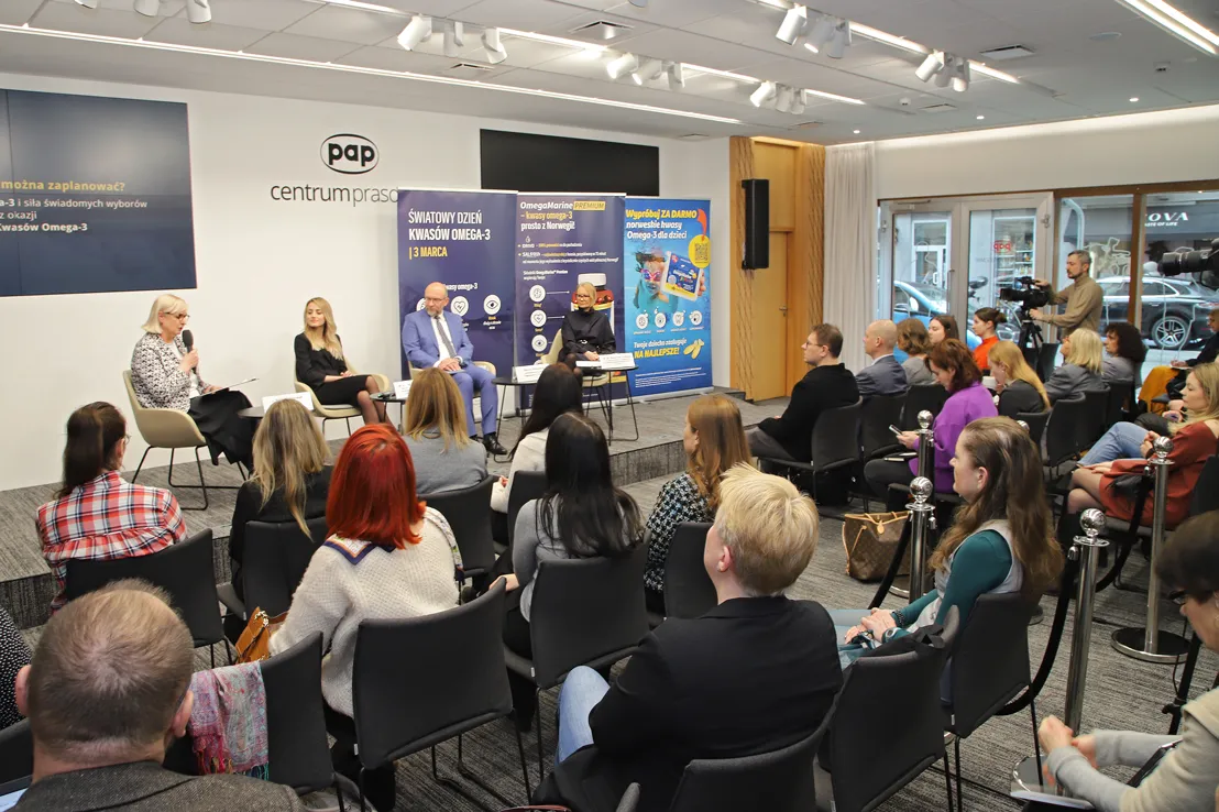Natural Pharmaceuticals OmegaMarine™ Premium Konferencja w centrum prasowym PAP: panel dyskusyjny o Światowym Dniu Kwasów Omega‑3, prelegenci na scenie, banery tematyczne, publiczność i kamery.